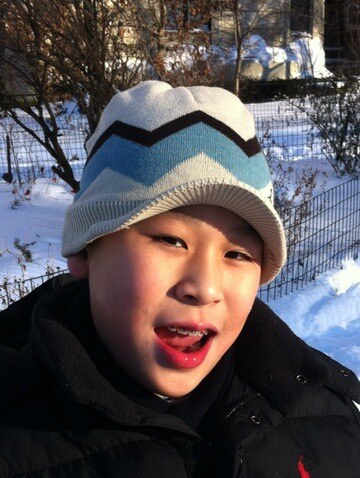 A childhood photo of Simon in a knit winter hat, smiling in the snow.